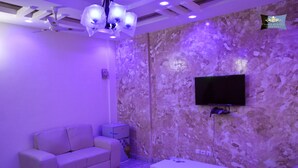 Ein modernes Wohnzimmer mit Wand im Marmor-Look, einem flachbildfernseher über einer weißen Unterhaltungsecke und einem beigefarbenen Sofa.