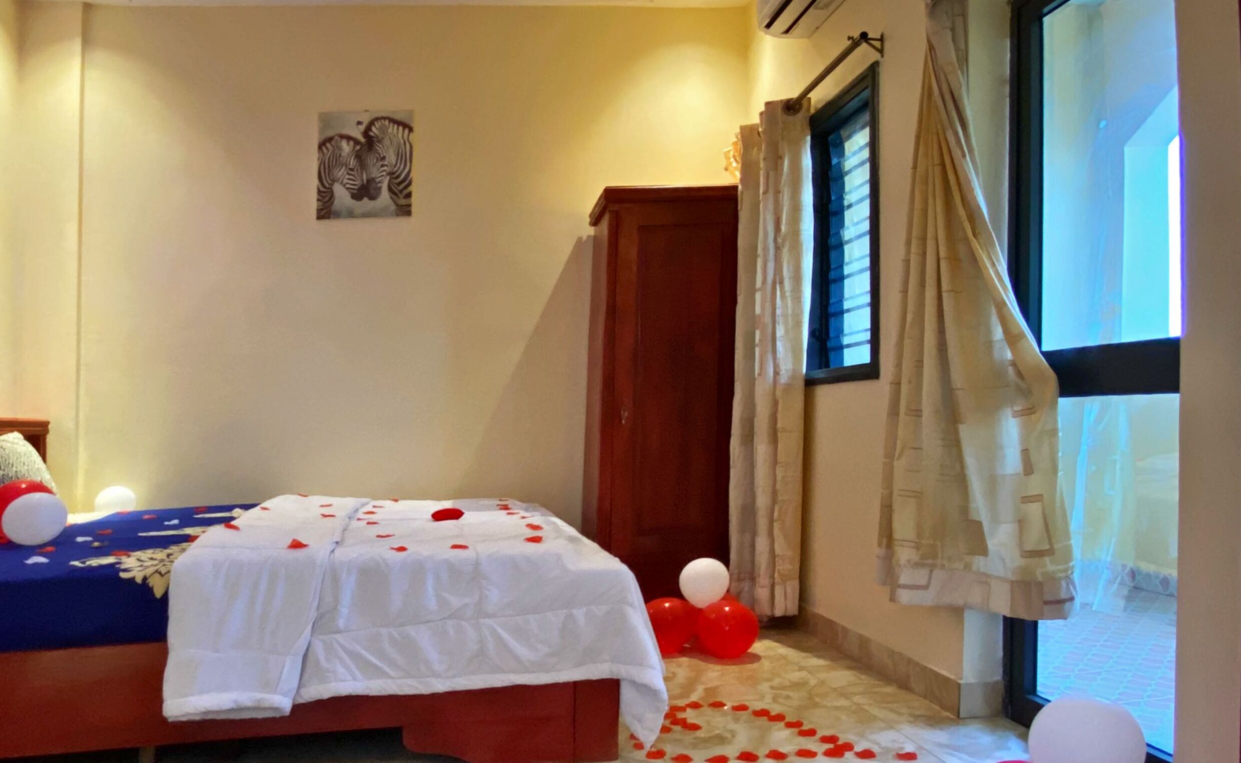 Une chambre à coucher avec un lit, un tableau représentant une zèbre accroché au mur, une fenêtre avec des rideaux et une porte.