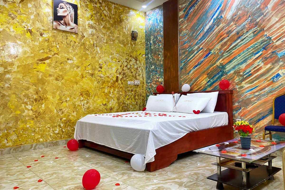 A hotel room with a bed, a wall with a painting, and a table with a vase of flowers.
