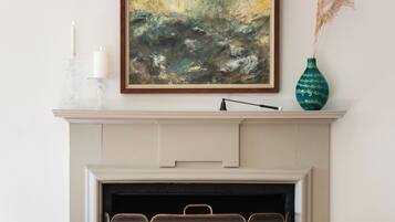A fireplace with a framed abstract painting above it, a vase with dried plants, and a decorative stand with candles.