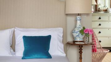 A neatly made bed with a colorful blanket, a teal pillow, and a bedside table with a lamp and vase of flowers.
