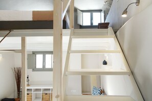 Ein mehrgeschossiges Interieur mit einer Holztreppe, weißen Wänden und einem Fenster, das natürliches Licht hereinlässt.