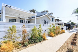 Un quartier résidentiel moderne, avec une clôture blanche, le numéro 2868, et une variété de plantes le long du trottoir.