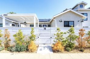 Une maison moderne à deux étages, avec une façade blanche, un patio couvert et une entrée sécurisée par un portail.