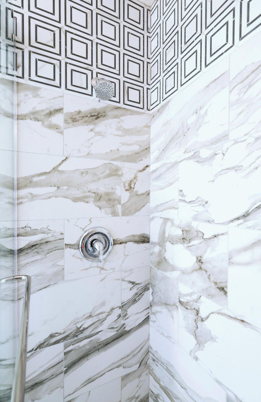 A shower with a marble wall and a geometric pattern above the showerhead.