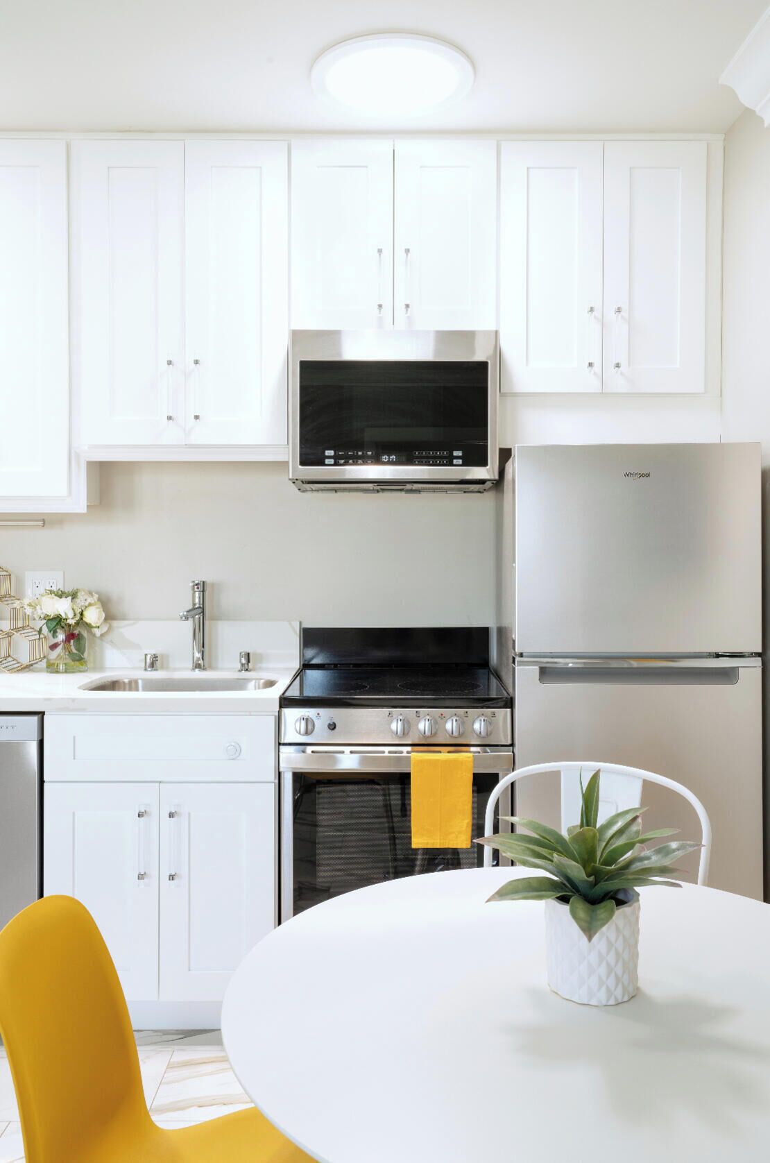 A modern kitchen with white cabinets, a stainless steel refrigerator, a stove, and a microwave.