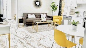 Una sala de estar moderna con un sofá, una mesa de centro y sillas amarillas. Hay una zona de cocina con armarios y una mesa de comedor.
