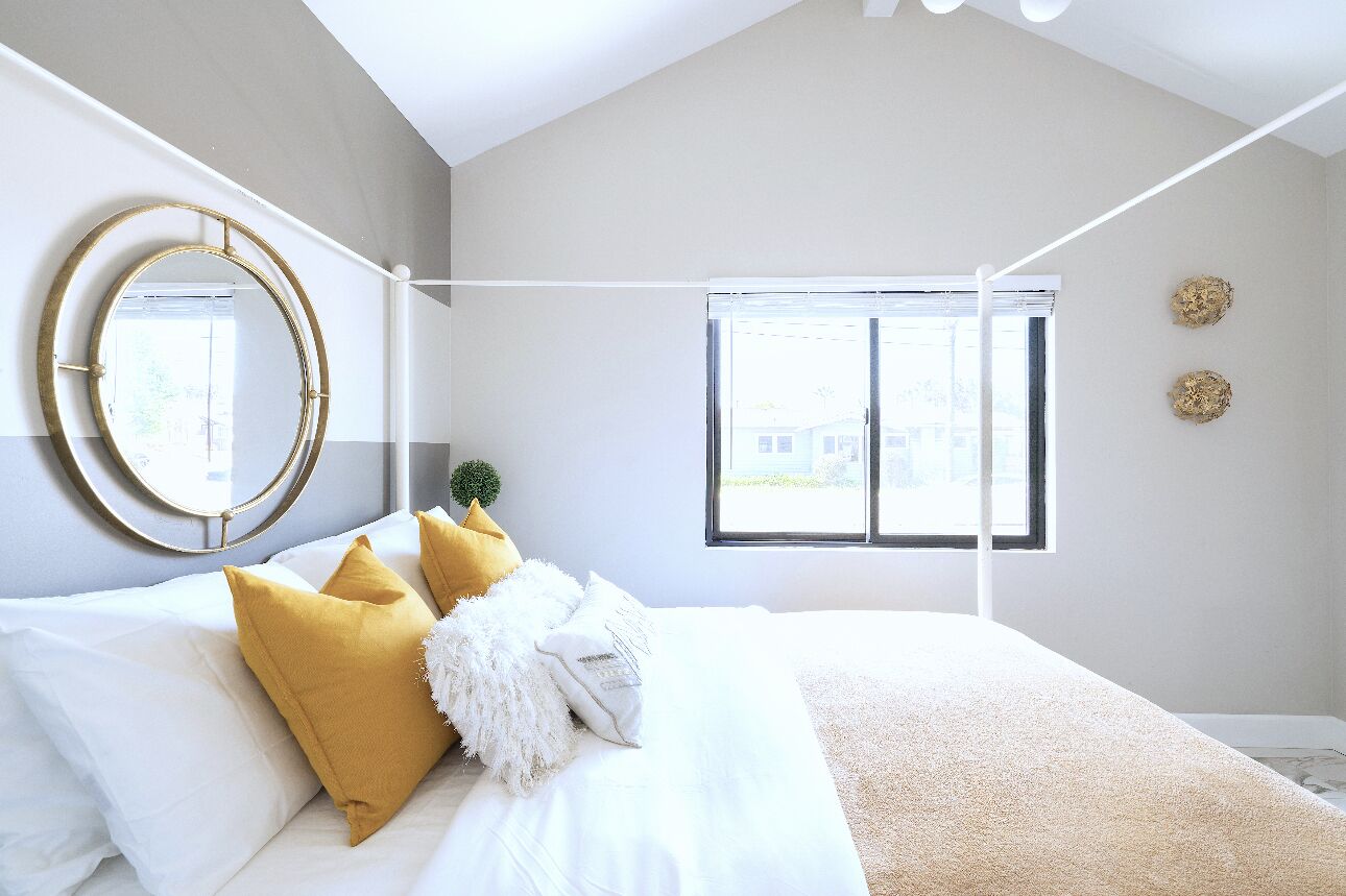 Ein Schlafzimmer mit einem Bett, einem runden Spiegel, einem Fenster und zwei Wandbildern.