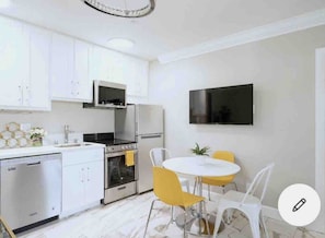 Une cuisine moderne avec des meubles blancs, une cuisinière et un lave-vaisselle. On y trouve également un coin repas avec une table blanche et des chaises jaunes.