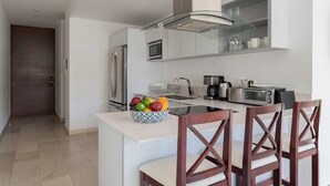 A modern kitchen with white cabinetry, a glass cooktop, and a bowl of fruit on the island. - Mexication Beach Bliss: Stylish Playa Getaway (Playa del Carmen)