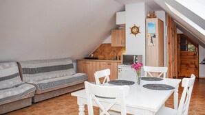 Un espace de vie chaleureux avec un canapé, une table à manger et des chaises, une cuisine en arrière-plan et une vue sur l’extérieur.