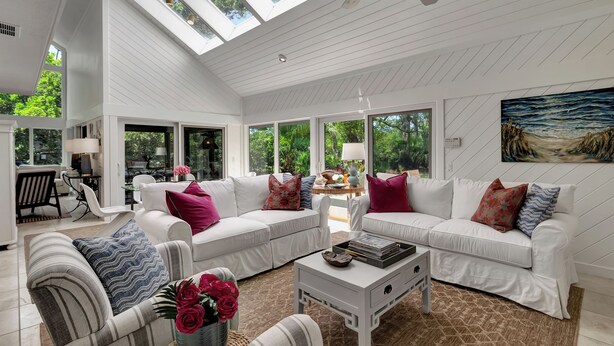 A spacious living room with white furniture, large windows, and a ceiling fan.
