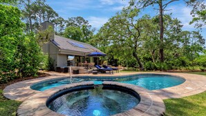 A backyard with a hot tub, a swimming pool, and a patio area with lounge chairs and a table.