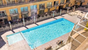 Ein rechteckiger Pool mit einer gefliesten Terrasse, umgeben von einem Metallzaun.