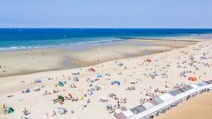 Ein Strand mit vielen Liegen und Sonnenschirmen, ein sandiger Uferbereich und ein klarer, blauer Himmel.