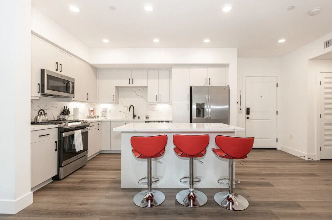 A modern kitchen with white cabinetry, stainless steel appliances, and a central island with red bar stools.