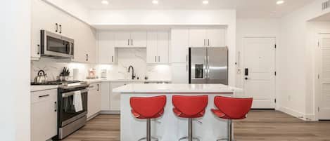 A modern kitchen with white cabinetry, stainless steel appliances, and a central island with red bar stools.
