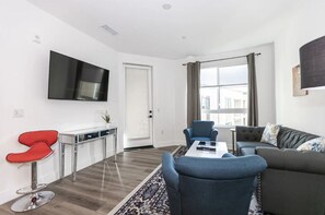 A modern living room with a grey sofa, blue armchairs, a coffee table, and a TV mounted on the wall. - Beach Condo 436CB (Carlsbad)