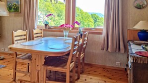 A wooden dining table with chairs, a vase with flowers, and a view of greenery through the window. - Cozy home in Lyngdal with kitchen (Lyngdal)