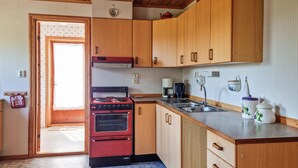 A compact kitchen with wooden cabinets, a red stove, a sink, and a coffee maker. - Cozy home in Lyngdal with kitchen (Lyngdal)