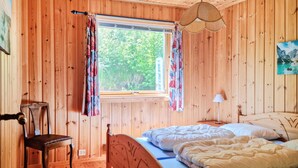 A wooden room with a bed, a chair, a window with curtains, a lamp, and a painting on the wall. - Cozy home in Lyngdal with kitchen (Lyngdal)