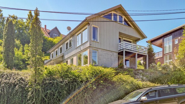 A modern two-story house with a balcony, surrounded by lush greenery and a car parked in front. - Cozy home in Lyngdal with kitchen (Lyngdal)