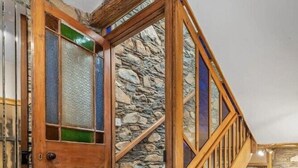 Een houten trap met een stenen achtergrond, een houten deur met glas-in-loodpanelen, en een metalen leuning.
