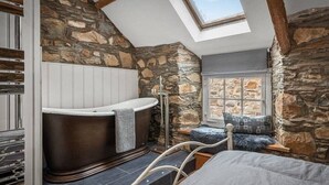 Een slaapkamer met een stenen muur, dakraam, een groot bad en uitzicht op de natuur.