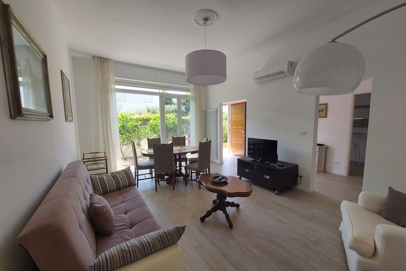 Un salon moderne comprenant un canapé, une table à manger et des chaises, un téléviseur et une grande fenêtre donnant sur un paysage verdoyant.