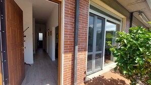 A modern building entrance with a wooden door, a brick wall, and a glass door leading to a covered patio area.