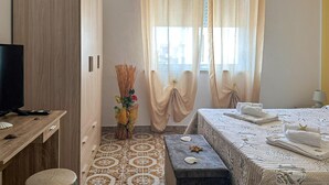 Una camera d'albergo con un letto, un comodino con una lampada, una TV e un vaso decorativo con piante secche.