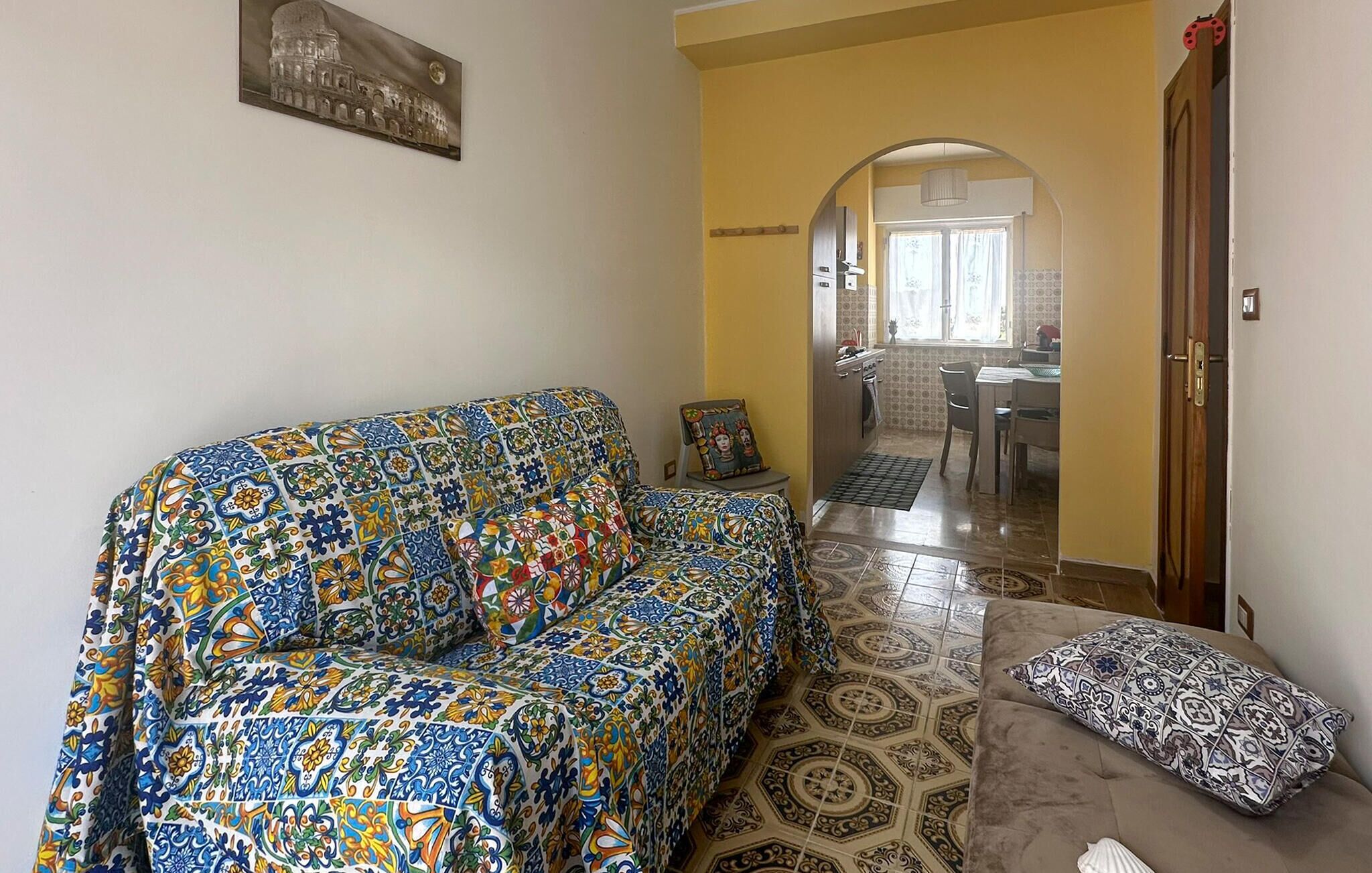 A living room with a patterned sofa, a patterned cushion, and a tiled floor.