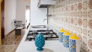 Una cucina con piano cottura a gas, lavello e piastrelle decorate. Sul ripiano ci sono tre contenitori gialli e blu.