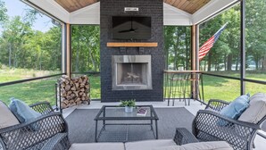 An outdoor patio with a stone fireplace, wicker furniture, and a view of the surrounding forest. - Our Sweet Little Piece of Tennessee  (Estill Springs)