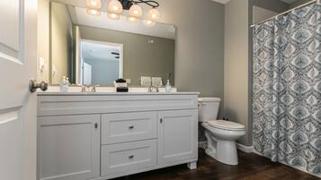 Une salle de bain avec un meuble-lavabo blanc, un miroir avec éclairage intégré, des toilettes et des rideaux de douche à motifs.