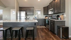 Una cocina moderna con gabinetes oscuros, electrodomésticos de acero inoxidable y una isla central con taburetes de bar.