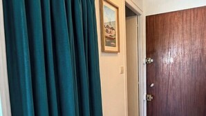A hallway with a wooden floor, a dark green curtain, and a wooden door with a light fixture above it.