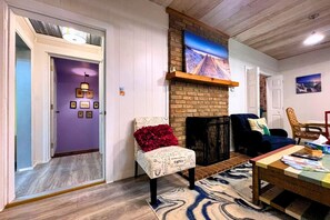 A room with a brick fireplace, a purple door, a chair with a red cushion, and a coffee table with books.