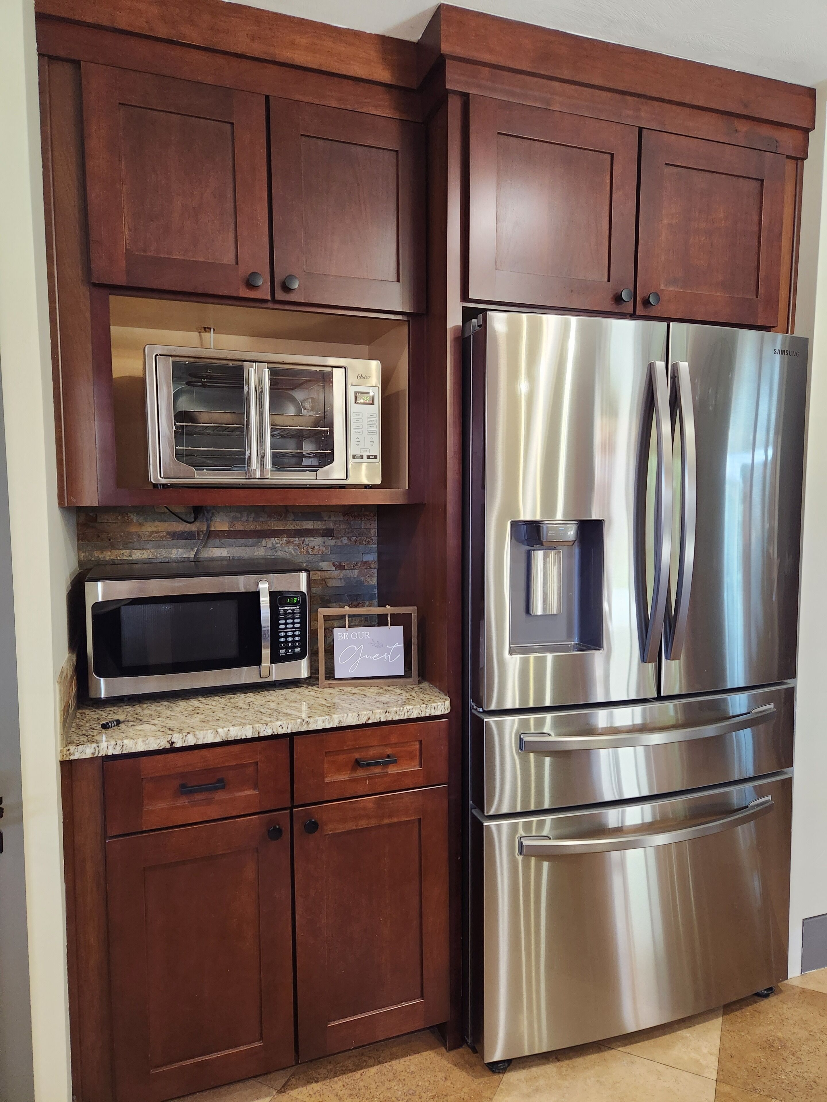 A kitchen with wooden cabinets, a stainless steel refrigerator, a microwave, and a toaster oven.