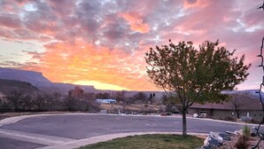 A parking lot with a tree and rocks in the foreground, a building with a red roof in the background, and a sunset sky. - Zion Happy Retreat- Game Room, Sauna, & workspace! Pet Friendly! (Toquerville)