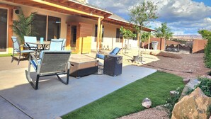 A covered patio with outdoor furniture, a stone fireplace, and a view of the surrounding landscape. - Zion Happy Retreat- Game Room, Sauna, & workspace! Pet Friendly! (Toquerville)