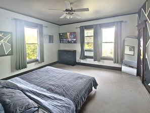 Ein Schlafzimmer mit einem Bett, einem Schminktisch, einem Fernseher und einem Deckenventilator.