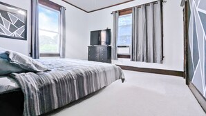 Ein Schlafzimmer mit Bett, Deckenventilator, Kommode und Fernseher.
