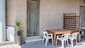 An outdoor patio with a wooden table and white plastic chairs, a potted plant, and a brick wall. - SE007 - Senigallia, one bedroom apartment on the sea with beach (Senigallia)