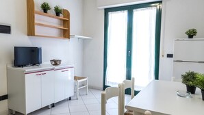 Eine moderne Küche mit weißen Schränken, einem Fernseher, einem Esstisch, Stühlen und einem Fenster mit Vorhängen.