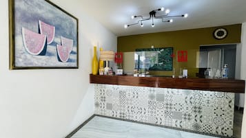 Een receptiegedeelte met een houten balie, een groot abstract schilderij, een moderne kroonluchter en betegelde vloeren.