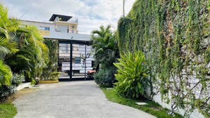 A pathway leading to a building with a gated entrance, surrounded by lush greenery and a white wall with climbing plants. - H.Ixaya (Puerto Vallarta)