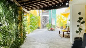 A covered walkway with a concrete floor, surrounded by potted plants and a seating area with a chair and table. - H.Ixaya (Puerto Vallarta)