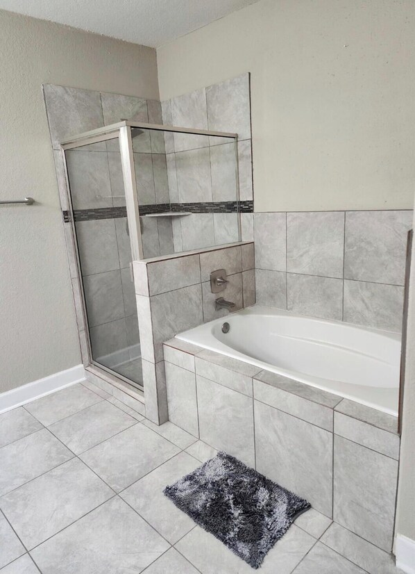 A bathroom with a shower enclosure, a bathtub, and a small rug.