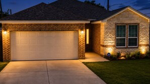 Uma casa com garagem, fachada de pedra e entrada iluminada.